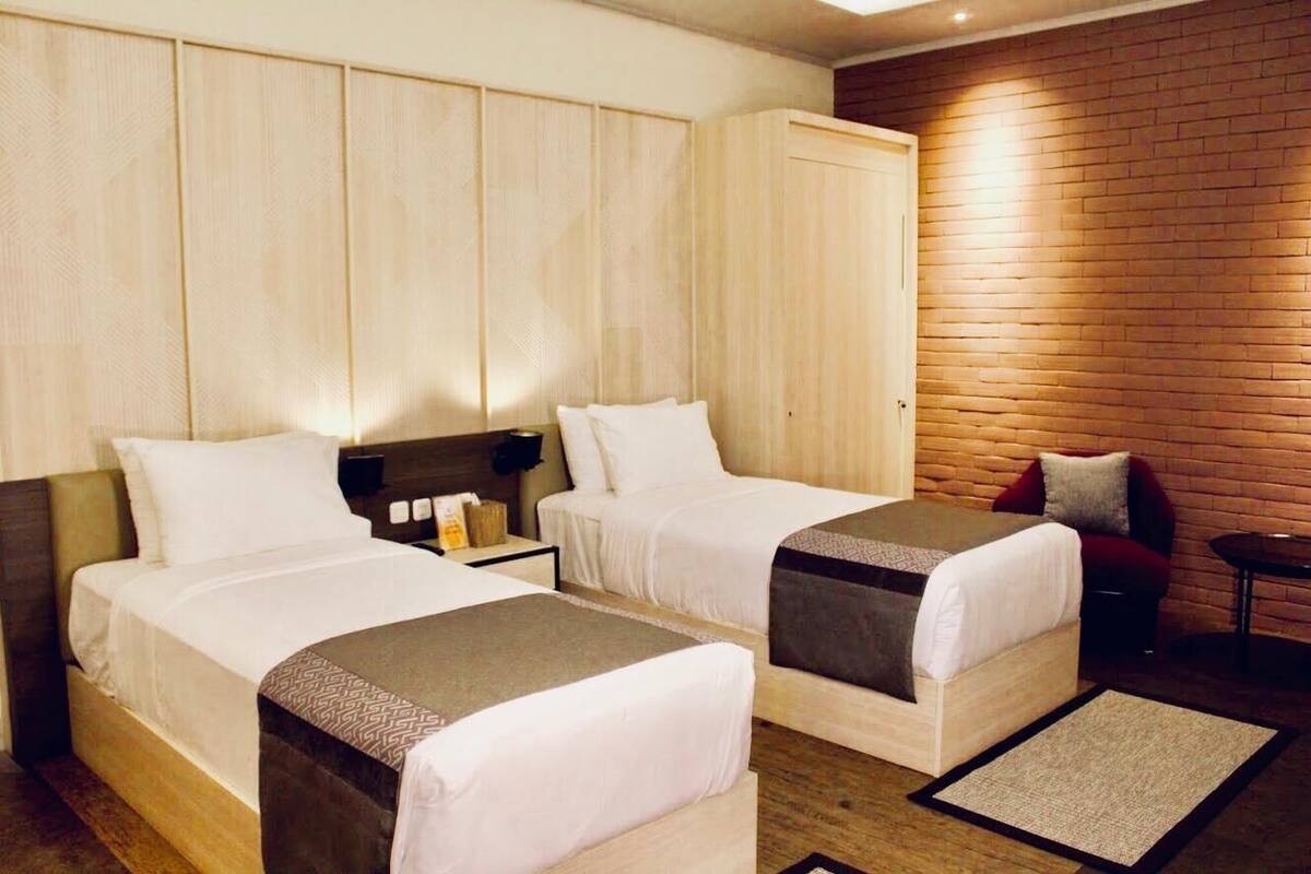 A hotel room with two beds, a wardrobe, a brick wall, and a small table.