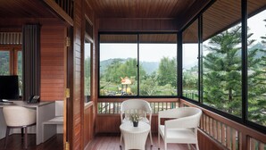 A wooden-paneled room with a desk, two chairs, and a large window offering a view of greenery and hills. - JSI Resort (Megamendung)