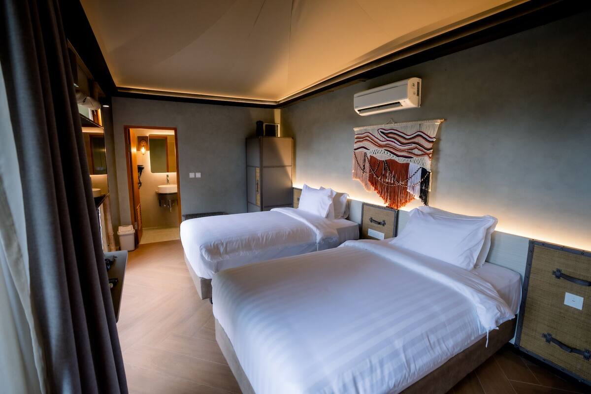 A hotel room with two beds, a bathroom, and an air conditioning unit.
