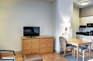 A compact living space with a TV on a wooden dresser, a dining table with chairs, and a kitchenette with a microwave. - Studio 6 New Orleans (New Orleans)