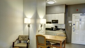 Une chambre d’hôtel compacte dotée d’une kitchenette, d’un coin repas avec deux chaises, d’une lampe et d’une porte avec une pancarte.