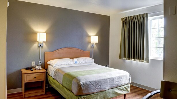 Une chambre d’hôtel avec un lit, des lampes de chevet, une table de nuit et une fenêtre avec des rideaux.