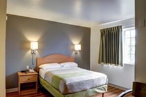 A hotel room with a bed, bedside lamps, a nightstand, and a window with curtains. - Studio 6 New Orleans (New Orleans)