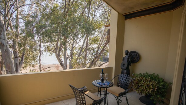 Un balcon avec une table et des chaises, un pot de fleurs et une vue sur des arbres et un immeuble.