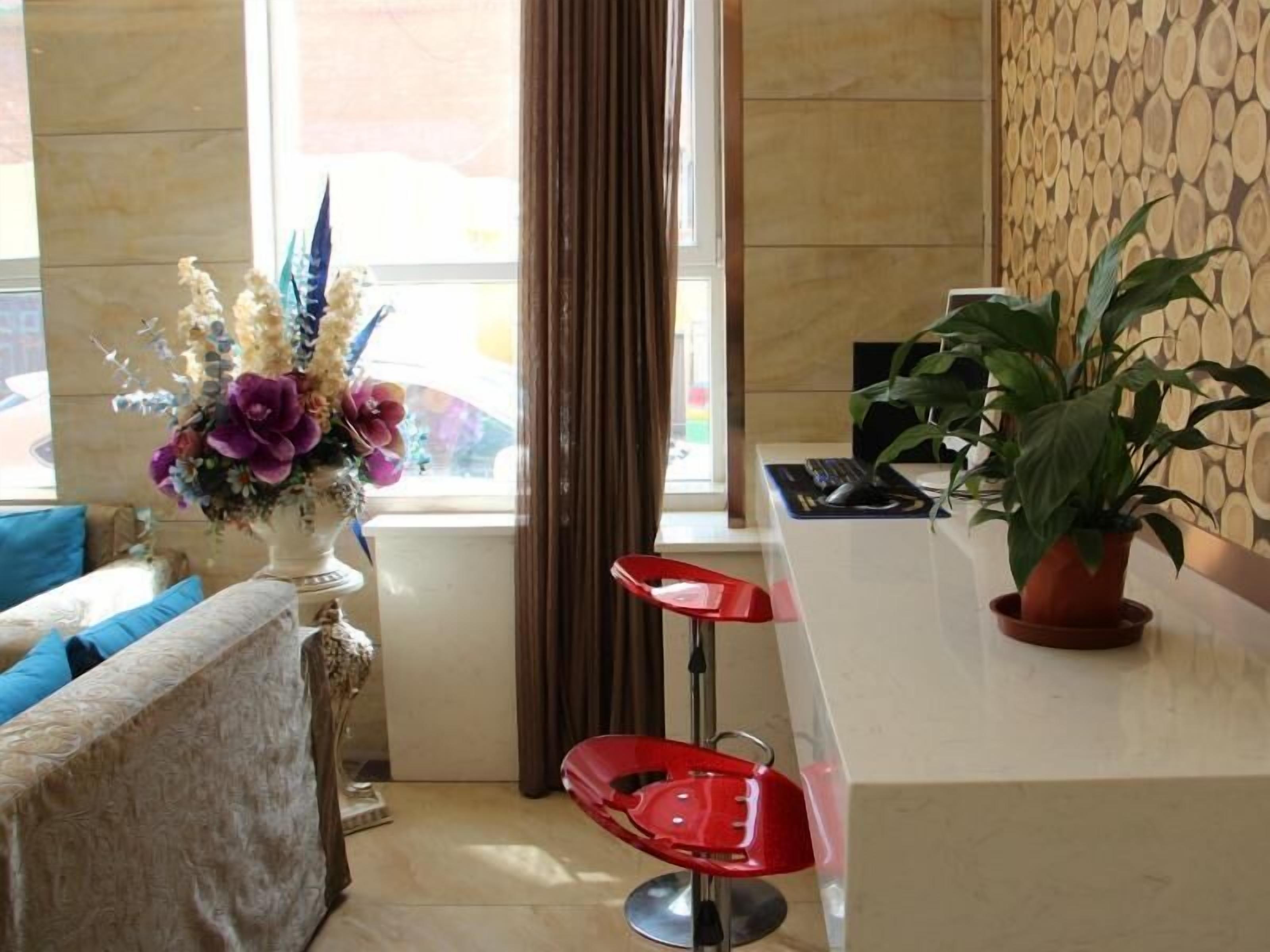 A modern hotel lobby with a seating area, a red chair, a vase of flowers, and a potted plant.