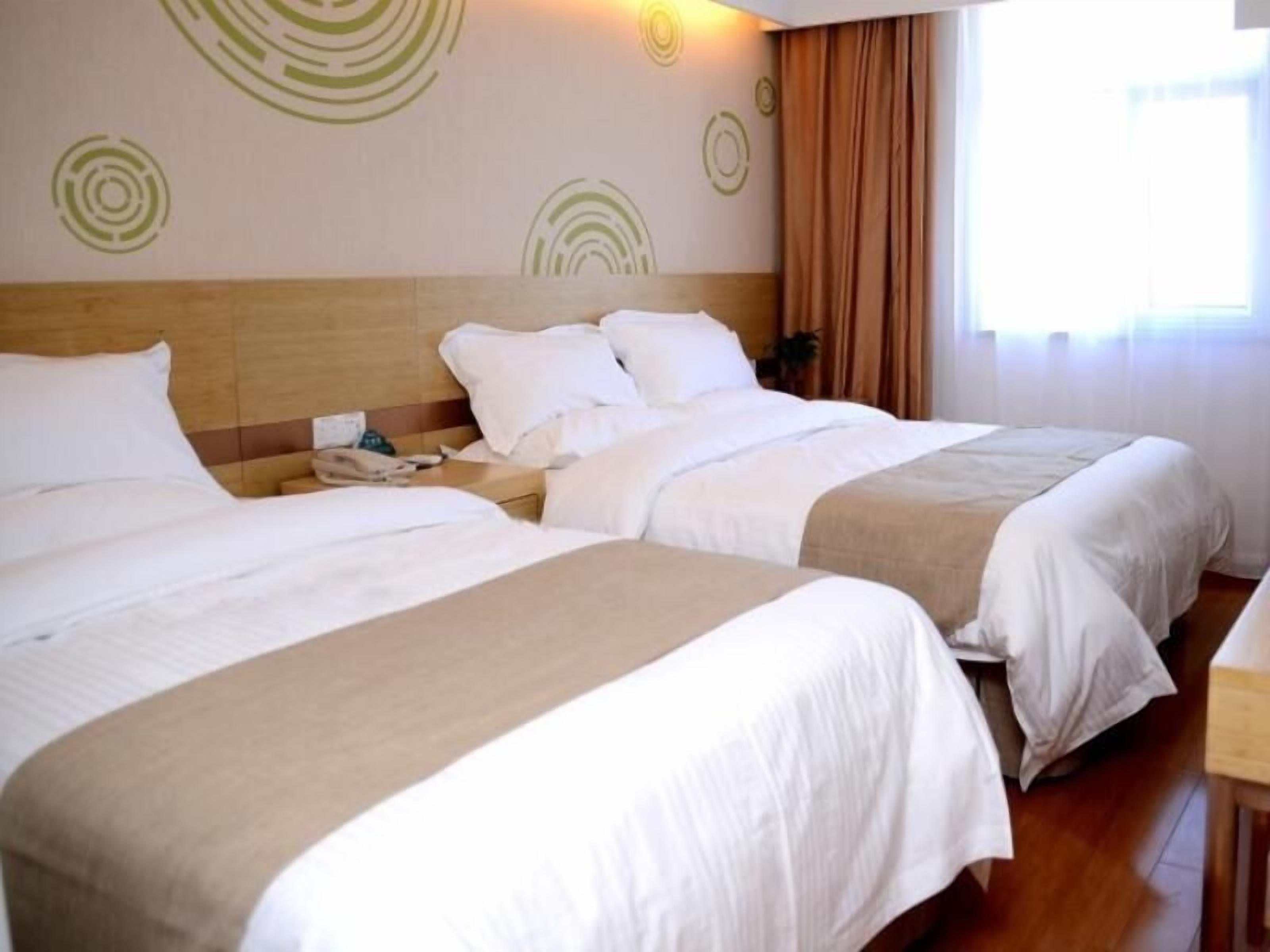A hotel room with two beds, a wooden headboard, a bedside table with a phone, and a window with curtains.