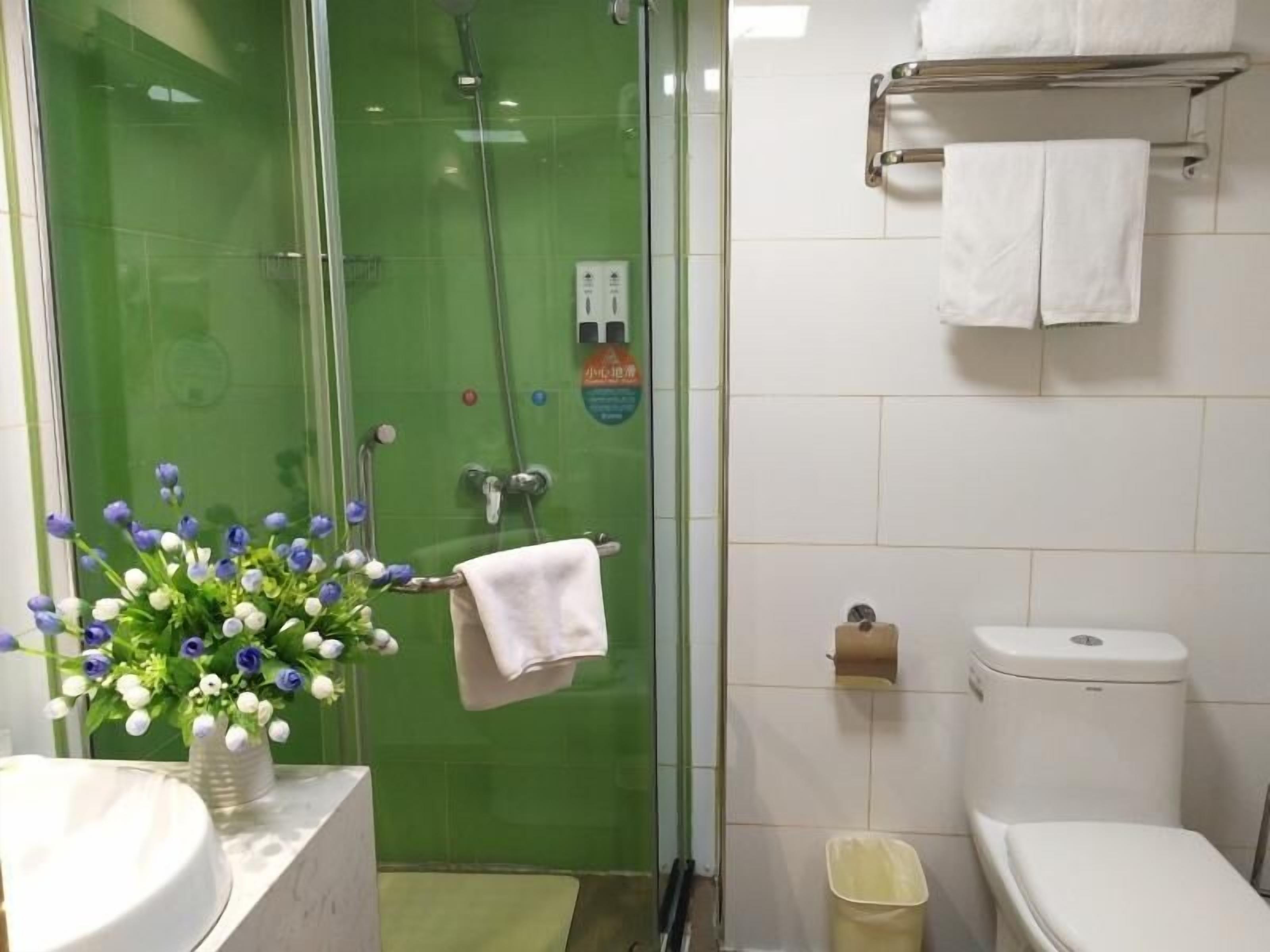 A bathroom with a glass shower enclosure, a toilet, a sink with a vase of flowers, and a towel rack.