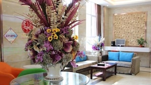 A lobby with a round glass table, a sofa, and a decorative vase with flowers.