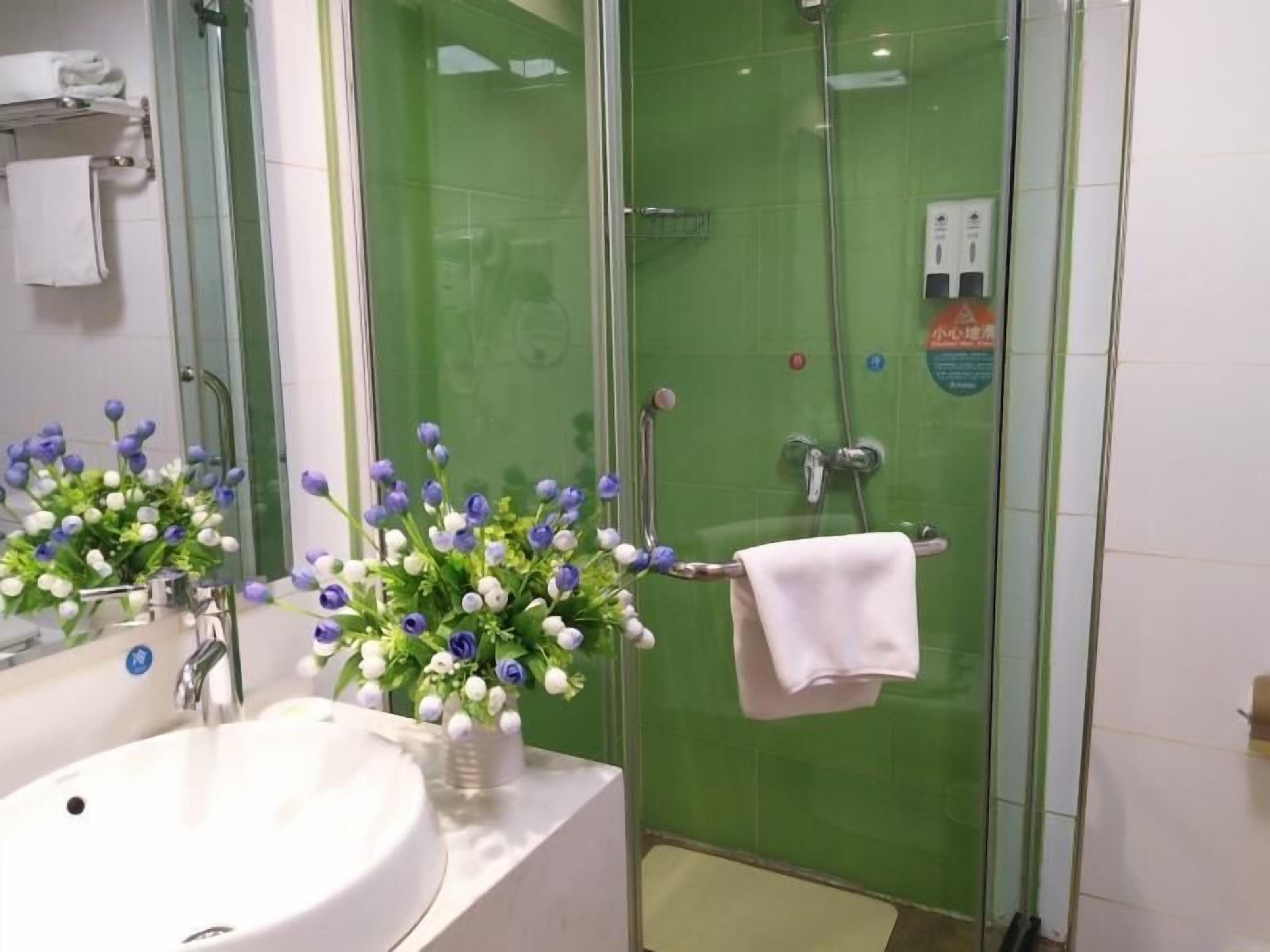 A bathroom with a white sink, a glass shower enclosure, and a vase of flowers on the counter.