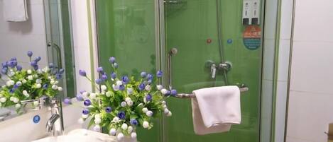 A bathroom with a white sink, a glass shower enclosure, and a vase of flowers on the counter.