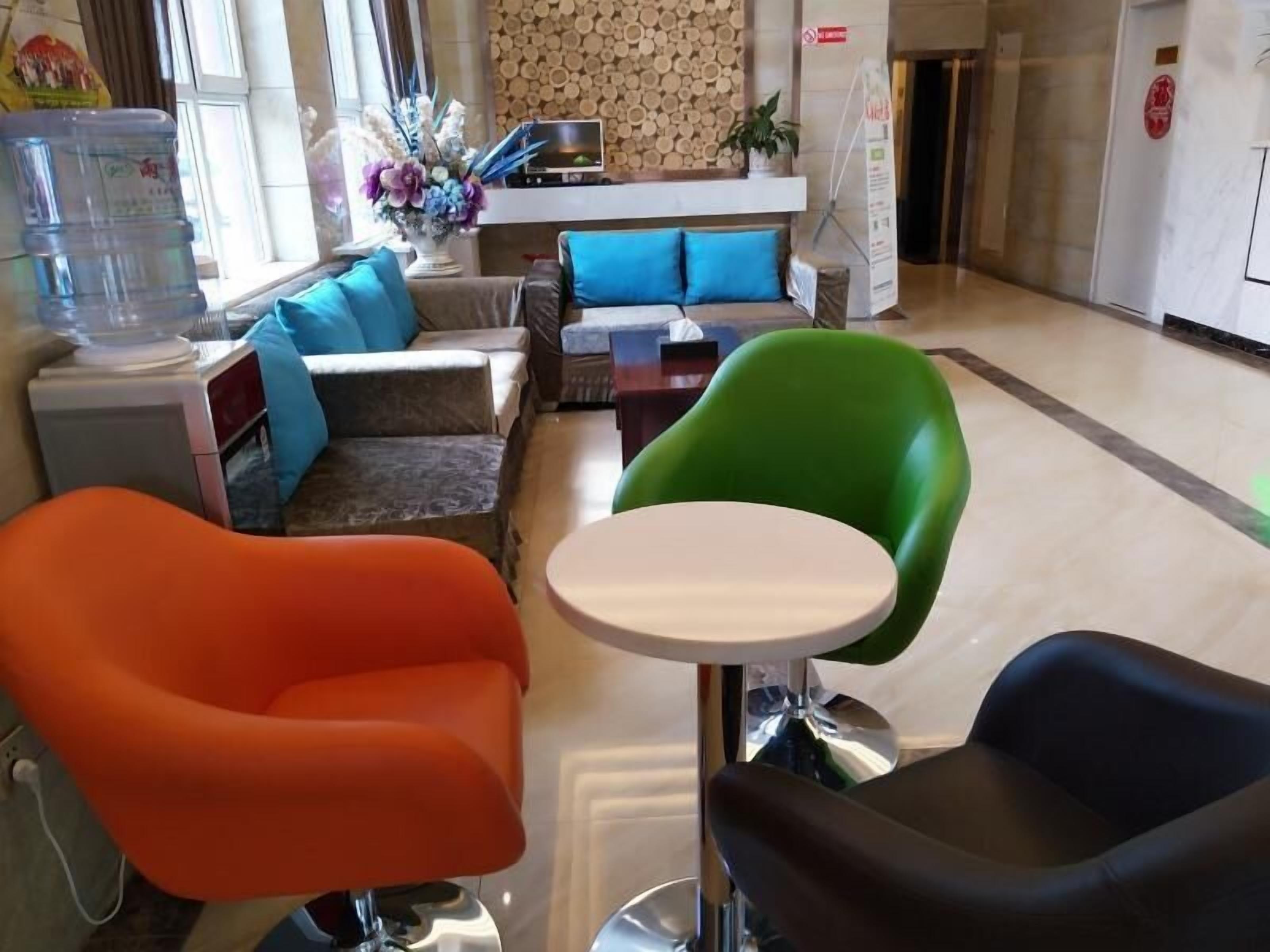 Um hall moderno de hotel com balcão de recepção, dispensador de água, sofá com almofadas azuis e cadeiras coloridas.