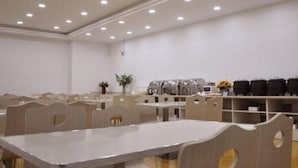A conference room with multiple tables and chairs, recessed ceiling lights, and a plant on the wall.