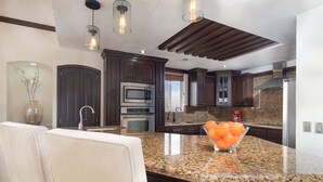 A modern kitchen with dark wood cabinets, granite countertops, stainless steel appliances, and pendant lighting. - Sonoran Sky Resort 310 Vacationer's Dream Getaway Ocean Front Condo (Puerto Peñasco)