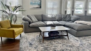 Una sala de estar con un sofá modular, un sillón amarillo, una mesa de centro y una planta grande en maceta.