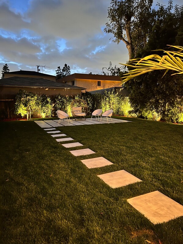 Un jardin avec un espace patio, des sièges et une pelouse bien entretenue.