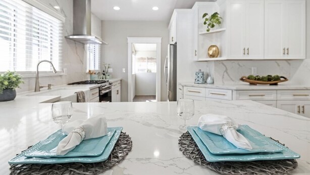 Una cocina moderna con armarios blancos, encimera de mármol y una isla central con un mantel tejido.