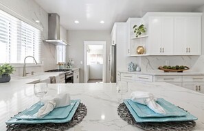 Une cuisine moderne avec des meubles blancs, un plan de travail en marbre et un îlot central agrémenté d’un set de table en fibres tressées.