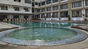 Un hotel con piscina rodeada de sillas de descanso y plantas en macetas.