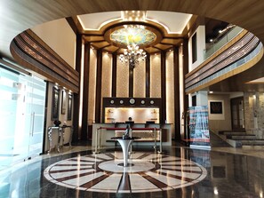 A lobby with a central reception desk, a chandelier, and a patterned floor.