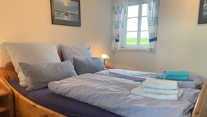 A neatly made bed with a wooden frame, a headboard, and a window with curtains. - Daggys Huus - Holiday home Daggy (Nordstrand)