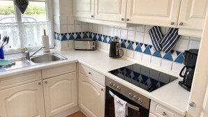 A kitchen with white cabinets, a black stove, a sink, and a window with a plant. - Daggys Huus - Holiday home Daggy (Nordstrand)