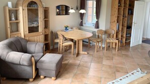 A cozy living room with a round wooden table, grey upholstered sofa, and wooden shelving units. - Daggys Huus - Holiday home Daggy (Nordstrand)
