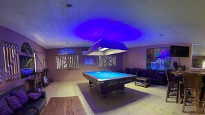 A pool table in a room with a wooden table and a sofa. - Monty's Riverside View Resort by Cocotel (San Antonio)
