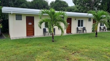 A small, single-story building with a flat roof, a front door, and a small porch area with two chairs and a table.