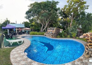 A swimming pool with a stone edge, surrounded by greenery and a gazebo.