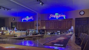 A bar area with a long counter, wooden cabinets, and a neon sign reading "Philippines." - Monty's Riverside View Resort by Cocotel (San Antonio)
