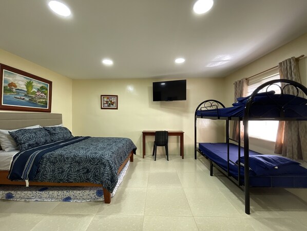 A bedroom with a bed, a desk, a bunk bed, and a TV on the wall.