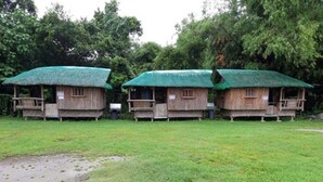 Three wooden cabins with green roofs and wooden balconies, surrounded by grass and trees. - Monty's Riverside View Resort by Cocotel (San Antonio)