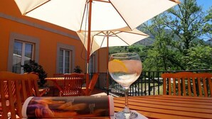 A wooden table with a glass of water and a magazine, an umbrella, and a view of trees and hills. - Picos de Europa (Cabrales)