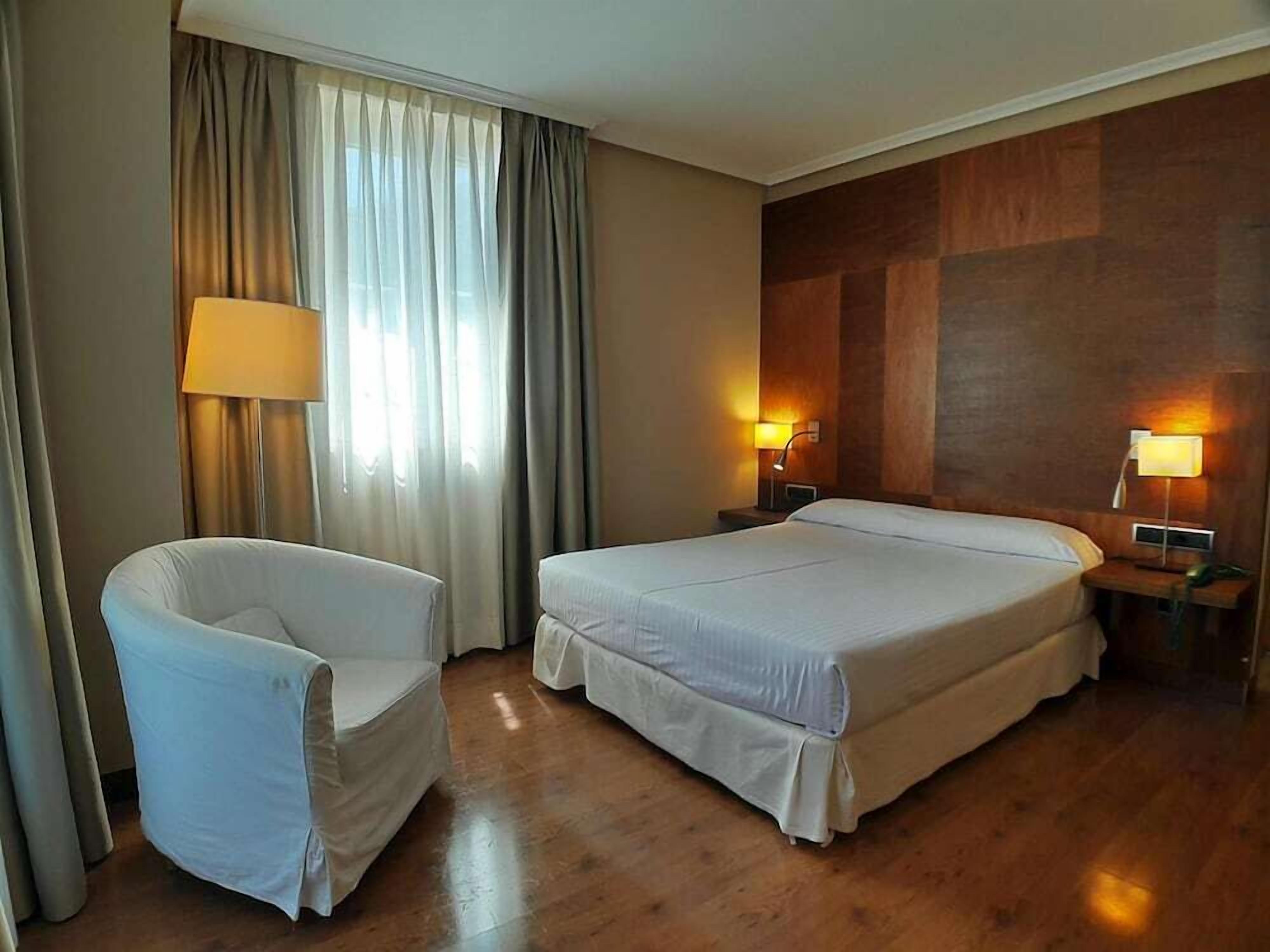 A hotel room with two beds, a chair, and two bedside lamps.