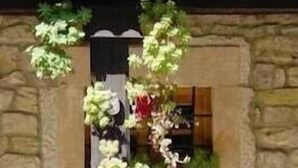 A stone building with a wooden post supporting hanging flower baskets. - Picos de Europa (Cabrales)