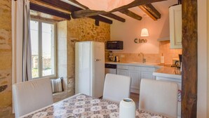 A rustic kitchen with stone walls, a white refrigerator, a microwave, and a sink. There's a dining table with chairs and a vase. - Cultural Treasure in Dordogne with furries (St. Medard D'excideuil)