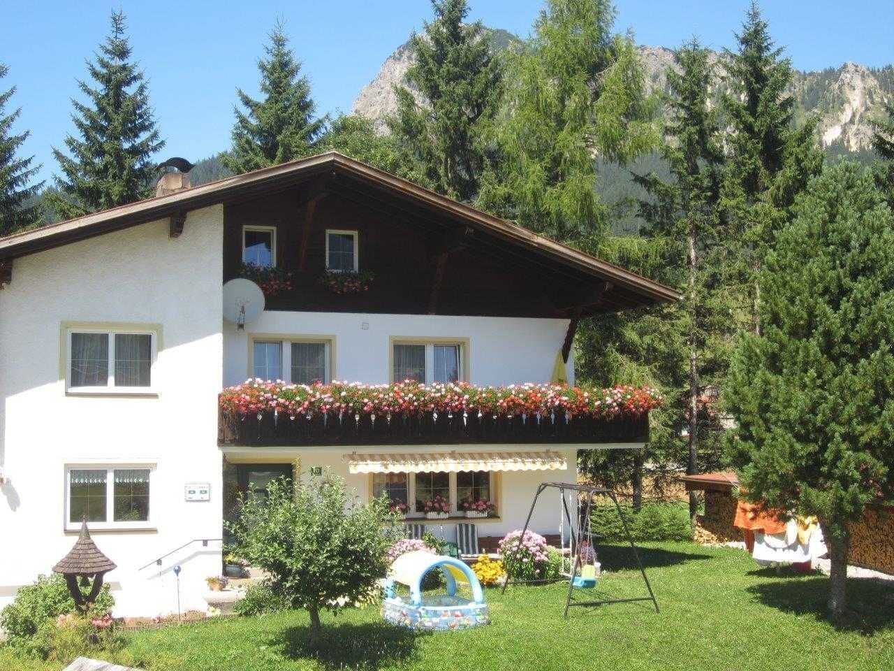 A two-story building with a balcony, surrounded by greenery and mountains.