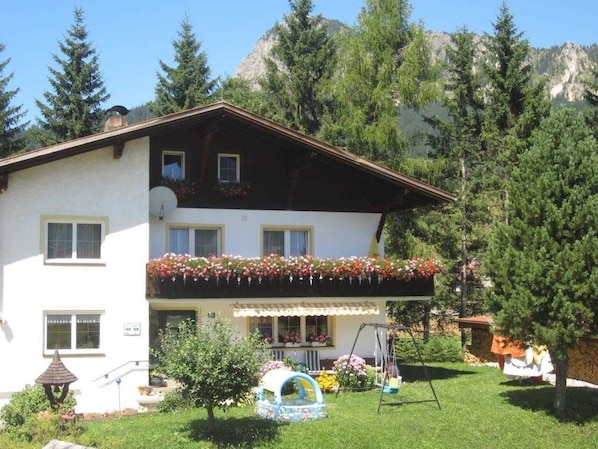 A two-story building with a balcony, surrounded by greenery and mountains.