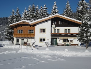 A two-story building with a wooden balcony, a satellite dish, and a snow-covered landscape.