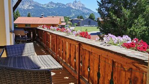 Eine Holzterrasse mit einem Korbstuhl, einem Holzzaun mit Blumen und Blick auf die Berge.