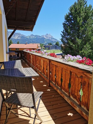 Eine Holzterrasse mit einem Korbstuhl, einem Holzzaun mit Blumen und Blick auf die Berge.