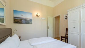 Une chambre à coucher avec un lit, un tableau, une lampe fixée au mur et une porte.
