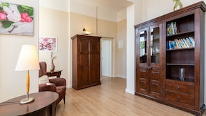 A spacious room with a wooden floor, a large wooden cabinet with books, a desk with a lamp, and a chair.