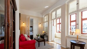 A spacious living room with a red sofa, a coffee table, and a view of the city through large windows.