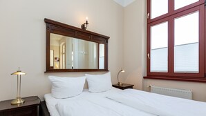 A neatly made bed with white linens, a bedside lamp, a nightstand, and a large mirror above the bed.