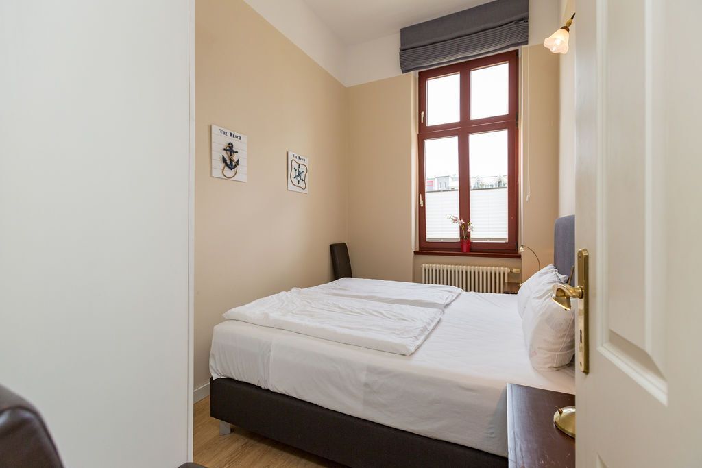 A bedroom with a bed, a window with blinds, and two framed pictures on the wall.
