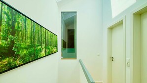 Un couloir orné d’une grande fresque représentant une forêt sur le mur de gauche, un passage étroit et une porte sur le mur de droite.