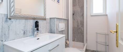 Une salle de bain avec un meuble-lavabo blanc, des toilettes, une douche et une petite fenêtre.