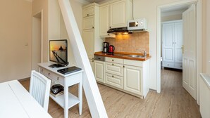 A compact kitchen with white cabinets, a microwave, and a coffee maker. There's a small dining area with a white table and chair. - Villa Amelia, App. 12 (Heringsdorf)