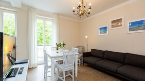 A living room with a dark grey sofa, a white dining table with chairs, a chandelier, and two framed pictures on the wall. - Villa Amelia, App. 12 (Heringsdorf)